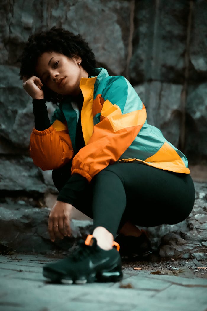 Afro-haired woman in vibrant jacket and black leggings sits on a Montreal street.