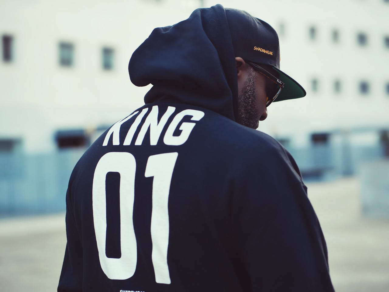 Man in a hoodie and cap with 'KING 01' during daylight in Lisbon.